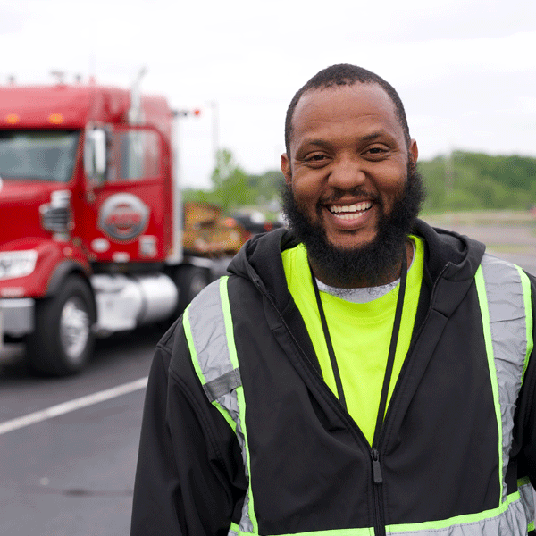 Smiling man standing in a parking lot in front of his red truck.